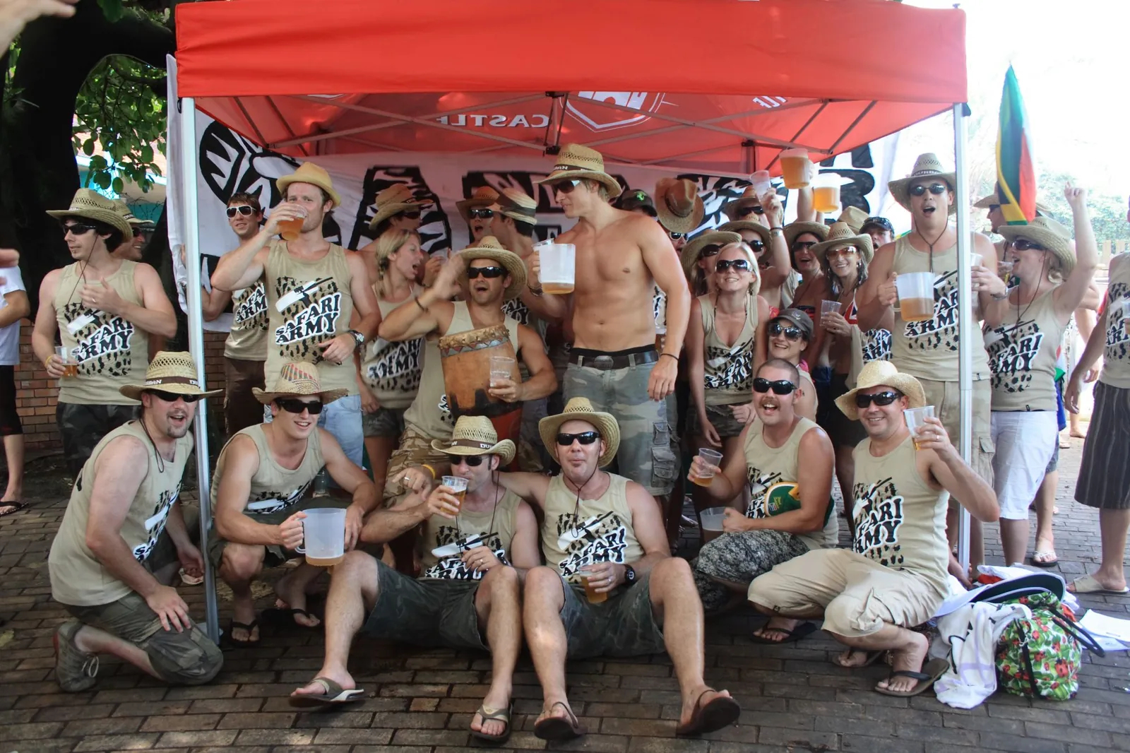 The Safari Army crew in matching vests and straw hats, raising jugs under a red gazebo