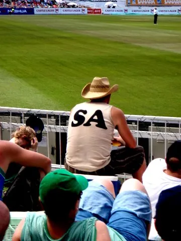 A fan in a straw hat and a vest with SA on the back, watching from the stands